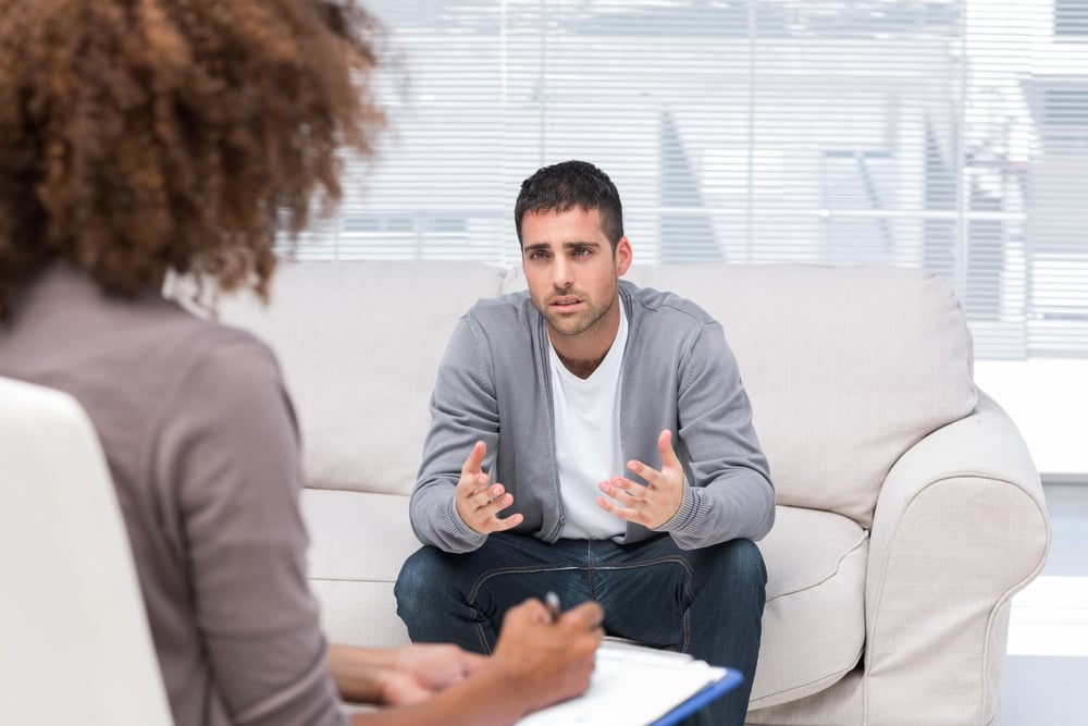 Depressed man speaking to a therapist while she is taking notes Depressed man speaking to a therapist while she is taking notes